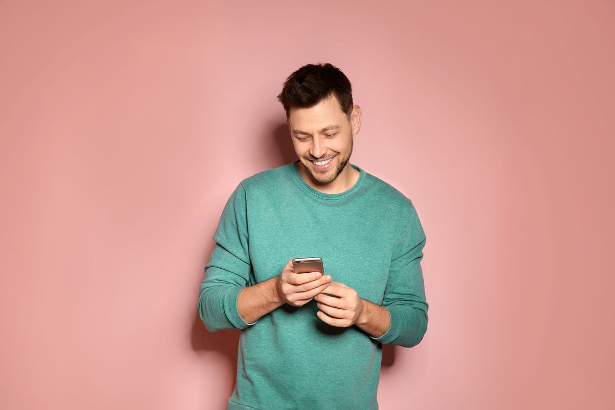 homme content sur son telephone fond rose coloré